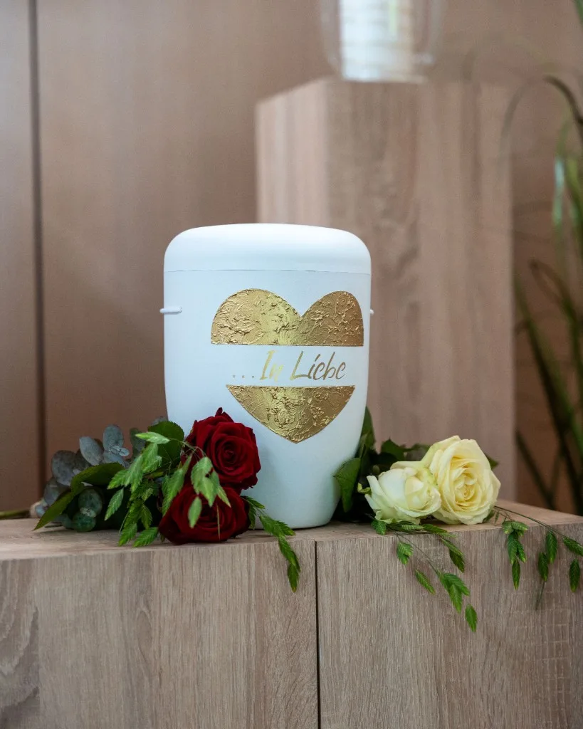 Urnenbestattung, weiße Urne mit goldenem Herz und Blumenschmuck